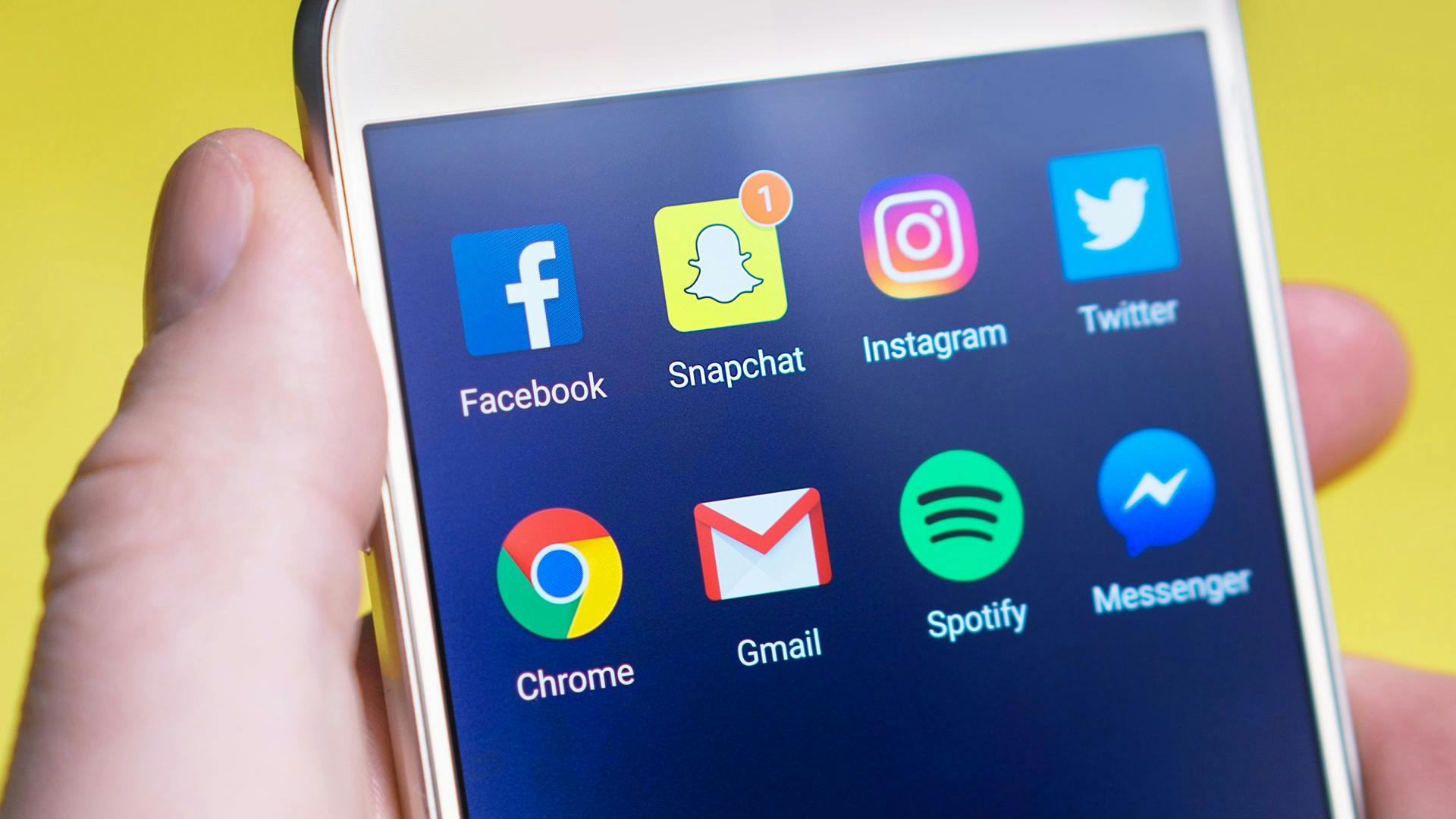 Smartphone with several apps on the screen over a yellow background.